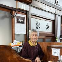 Sento co-owner Noriko Tsuchimoto sits at an antique counter, where she collects an entrance fee from bathers. | SATOKO KAWASAKI