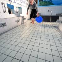 Yasuhiro Tsuchimoto, the fourth owner of the Inariyu sento, pours warm water over the floor when the facility opens in the early afternoon to keep bathers\' feet warm. | SATOKO KAWASAKI