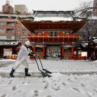 A man clears snow from a walkway at Kanda Miyojin Shrine on Monday. Tokyo\'s first snowstorm of the year disrupted many commuters and travelers. | REUTERS