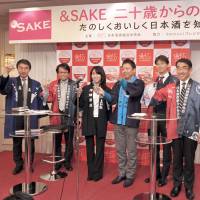 Koichi Saura (right), president of Saura Co. and chairman of the sake sales promotion committee of the Japan Sake and Shochu Makers Association, along with representatives of the sake industry and committee members, share a toast to kick off an event featuring sake tasting, cooking and education for about 100 twenty-year-olds celebrating Coming-of-Age Day. | YOSHIAKI MIURA