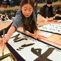 Akira Shoyama writes traditional calligraphy during an annual New Year\'s calligraphy contest in Nippon Budokan Hall in Tokyo on Tuesday. Some 3,115 participants, from preschool age to 92, took part. | SATOKO KAWASAKI