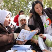 A Japan International Cooperation Agency volunteer shows a health handbook created for pregnant women and children to a woman in Palestine. | JICA