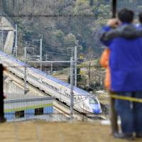 Railway fans watch a Hokuriku bullet train pass by in Tsubata-machi, central Ishikawa Prefecture, in March 2015. | KYODO