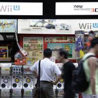 Pedestrians walk past signage advertising Nintendo products outside an electronics store in Tokyo. | BLOOMBERG