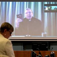 Senior Counsel Assisting Gail Furness stands in front of a screen displaying Australian Cardinal George Pell as he holds a Bible while appearing via video link from a hotel in Rome to testify at the Australia\'s Royal Commission into Institutional Response to Child Sexual Abuse in Sydney on Monday. Pell said on Sunday the Catholic Church had made \"enormous mistakes\" as he became the highest-ranking Vatican official to testify on sexual abuse of children in the Church. | REUTERS / JEREMY PIPER-OCULI/HANDOUT VIA REUTERS