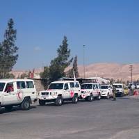 A humanitarian aid convoy consisting of the Red Cross and Syrian Arab Red Crescent wait to deliver aid at the entrance of the insurgent-held town of Mouadamiya, southwest of Damascus, Feb. 3. | REUTERS