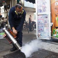 A worker from the Chacao municipality sprays insecticide into a sewer to eradicate mosquitoes that can cause the Zika virus in Caracas on Tuesday. | BLOOMBERG