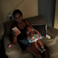 Vanessa, 32, types a text message on her mobile phone as she holds her daughter, Valentina, who is 5-months-old and was born with microcephaly, inside of their house in Jaboatao, near Recife, Brazil, Friday. | REUTERS