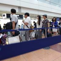 Passengers wait in line at an All Nippon Airways check-in counter at Haneda airport in Tokyo in August 2015. | BLOOMBERG