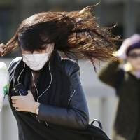 Pedestrians brave strong winds on Sunday in Minato Ward, Tokyo. | KYODO