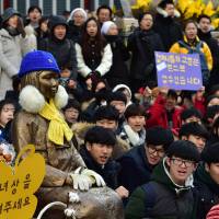 South Korean students sit near a statue of a teenage girl symbolizing former “comfort women” during the weekly demonstration in front of the Japanese Embassy in Seoul on Wednesday. | AFP-JIJI