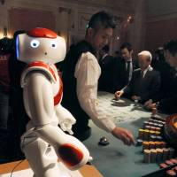 A robot helps a dealer at a mock casino at the Huis Ten Bosch theme park in Sasebo, Nagasaki Prefecture, on Tuesday. \"No more bets!\" was among the phrases the robot uttered. The ruling coalition is expected to shelve a bill that would allow resort facilities to run casinos until after the Upper House election in the summer. | KYODO