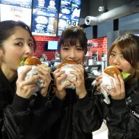 Models bite into Carl\'s Jr. burgers at the U.S. fast food chain\'s new outlet in Tokyo\'s Akihabara district on Wednesday. | KAZUAKI NAGATA