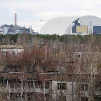 A containment shelter for the damaged fourth reactor (left) and the New Safe Confinement (NSC) structure (right) at the Chernobyl Nuclear Power Plant are seen from Ukraine’s abandoned town of Pripyat Wednesday. As 30th anniversary of Chernobyl nears, giant arch set to encase radiation for next 100 years