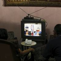 A couple watch television as U.S. President Barack Obama (left) and his Cuban counterpart, Raul Castro, hold a joint news conference in Havana Monday, and undergo tough questioning by reporters. Cubans glued to sets to view rare press grilling of Castro, Obama