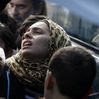 A refugee woman is pushed while waiting with others to receive food packages provided by humanitarian workers at a makeshift camp near the northern Greek border post of Idomeni on Friday. | AP