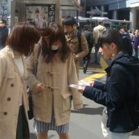 A volunteer member of the Osaka-based group Chikan Yokushi Katsudo Center distributes badges developed to warn would-be gropers on trains in Shibuya, Tokyo, on Friday. | DAISUKE KIKUCHI