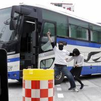 A man playing the role of a bus hijacker holds up a mock pistol next to a woman playing a hostage while members of the Emergency Response Team simulate a bus hijacking and hostage crisis during a drill at a bus terminal in Shinjuku, Tokyo, on Wednesday. | BLOOMBERG