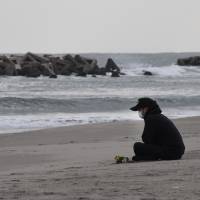 A man prays for victims of the 2011 earthquake and tsunami on a beach in Sendai, Miyagi Prefecture, on March 11, 2016. | AFP-JIJI