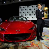 Masahiro Moro, president of Mazda Motor Corp.\'s North American Operations, holds the trophy for World Car of the Year 2016 next to the new Mazda MX-5 Miata at the New York International Auto Show on Thursday. | REUTERS