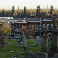 The blast furnaces of the now-closed Bethlehem Steel mill sit behind row houses and a cemetery in Bethlehem, Pennsylvania, Thursday. After Bethlehem Steel\'s blast furnaces went silent 20 years ago in the city of Bethlehem, the local economy bounced back as new industrial parks filled with e-commerce companies and white-collar businesses fleeing New York\'s higher costs. | REUTERS