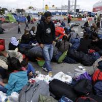 Migrants with their belongings wait for a bus transporting them to government-built shelters from the Athens port of Piraeus on Monday. More than 53,000 people who made their way to Greece from Turkey have been stranded in the country since Balkan and European nations shut their land borders to stem the largest refugee flow the continent has seen since World War II. | AP