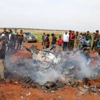 Rebel fighters and civilians gather around the wreckage of a Syrian warplane that was shot down in the Talat al-Iss area, south of Aleppo, Syria, on Tuesday. | REUTERS