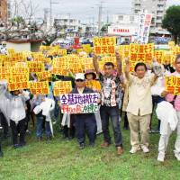 Protesters put up yellow signs saying \"Let\'s take back Futenma\" Sunday near the Futenma base in Ginowan, Okinawa Prefecture. | KYODO