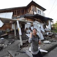 A couple head home past a severely damaged house in Mashiki, Kumamoto Prefecture, on Saturday. | AFP-JIJI