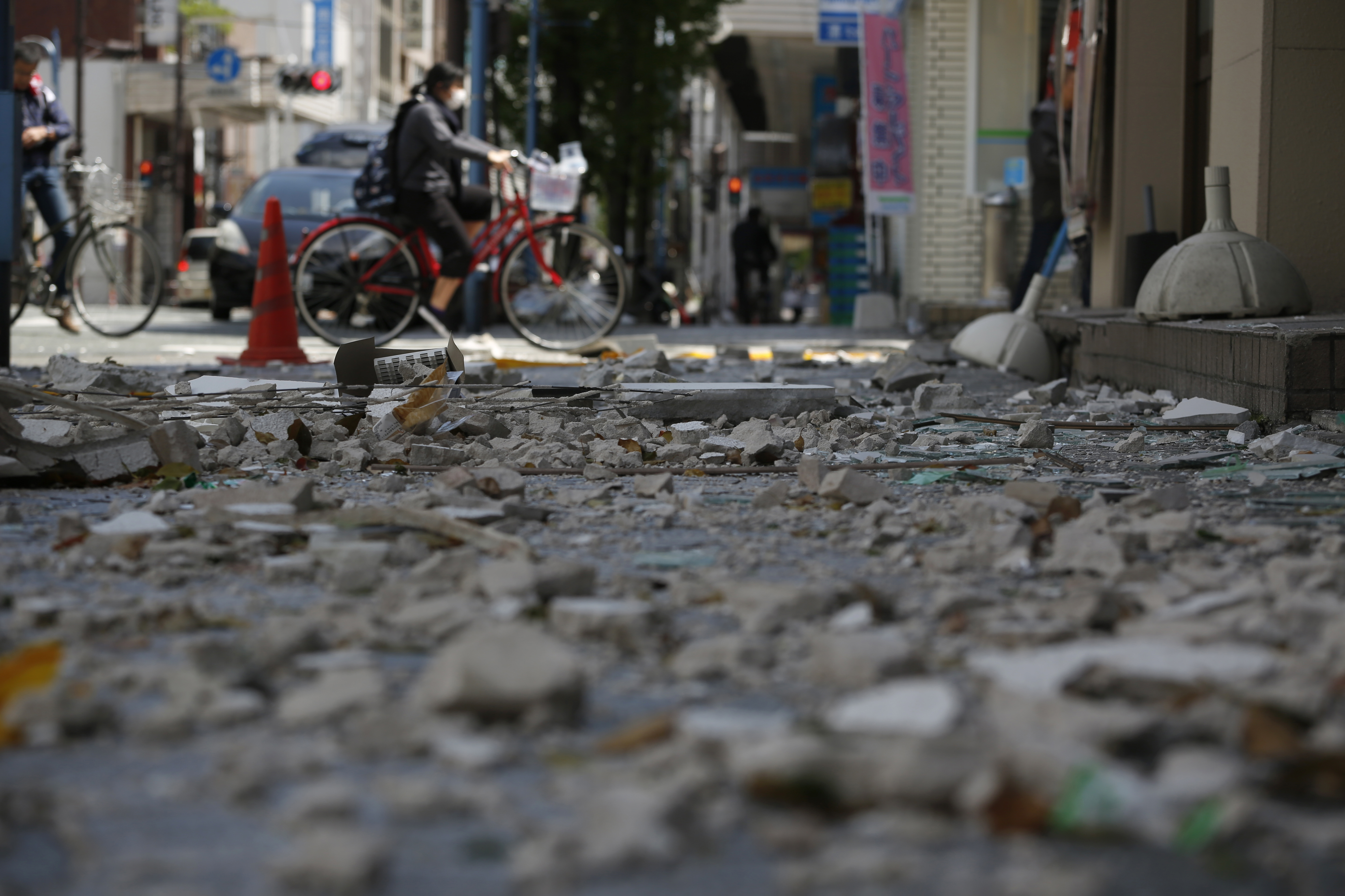 A cyclist passes by the debris at an arcade street in Kumamoto city on April 17, 2016. | AP