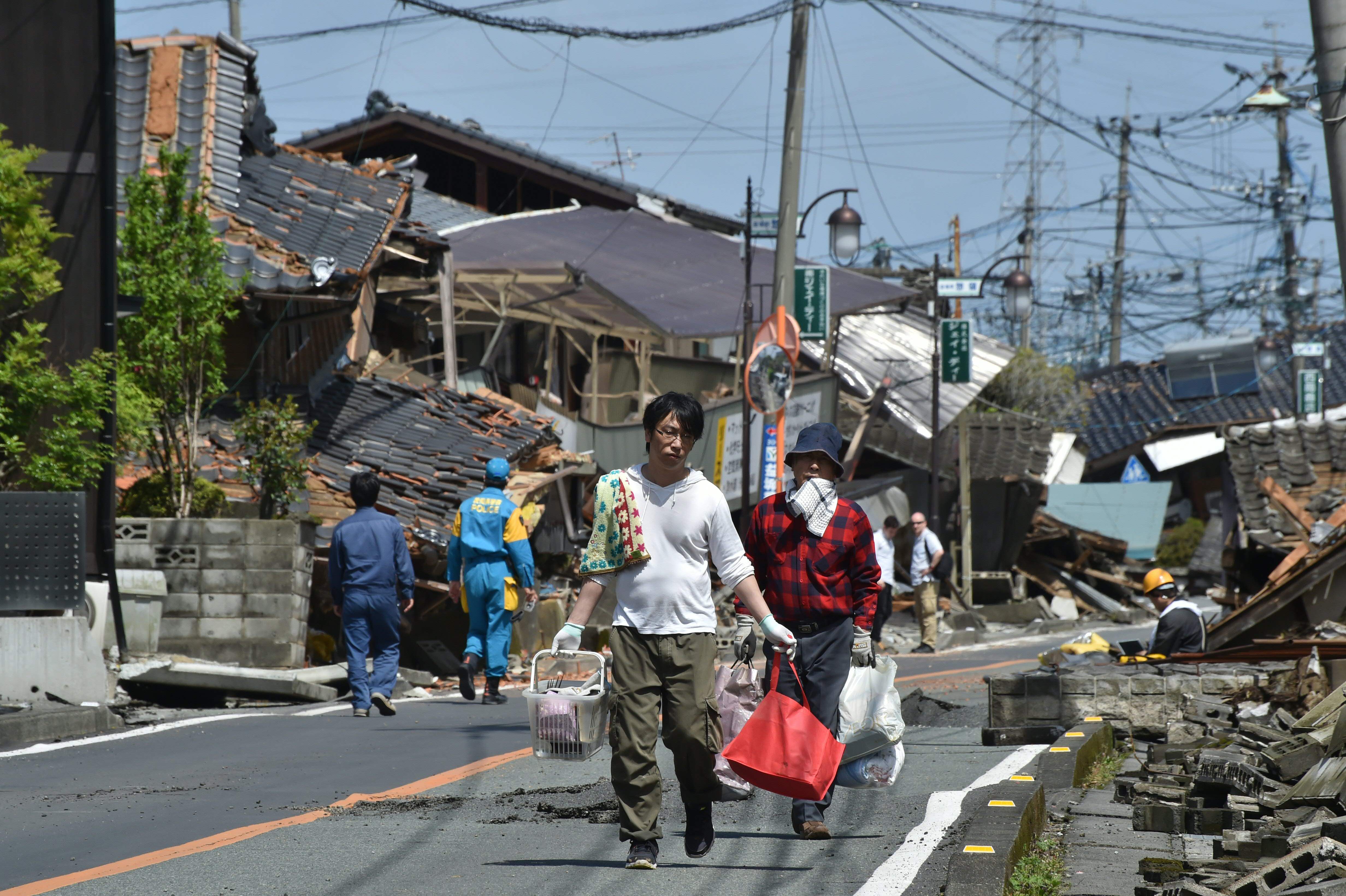 Residents walk on a street next to houses destroyed in the recent earthquakes in Mashiki, Kumamoto Prefecture. on April 17, 2016. | AFP-JIJI