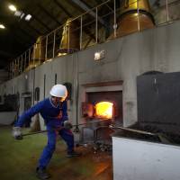 Fire in the hole: A worker (left) tends the coal fire under a still at Nikka Whisky Co. in Yoichi, Hokkaido, carefully maintaining just the right heat for perfect distillation. All the smoke is cleaned of soot and harmful toxins before it is released into the air. | BLOOMBERG