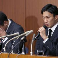 Kento Momota speaks as Kenichi Tago cries into a handkerchief during a news conference on Friday. | AP