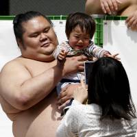 A sumo wrestler hold up a child, who might not be such a big fan now but give it time. | REUTERS
