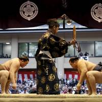 A referee stands between Mongolia-born grand sumo champions Hakuho (left) and Kakuryu  as they face off before a exhibition bout. | REUTERS