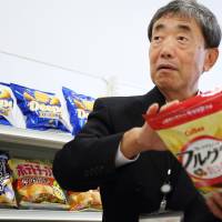 Akira Matsumoto, chief executive officer of Calbee Inc., holds a package of the firm’s popular granola.  | BLOOMBERG