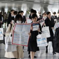 University students hold floor maps as they walk through a job fair in Tokyo. | BLOOMBERG