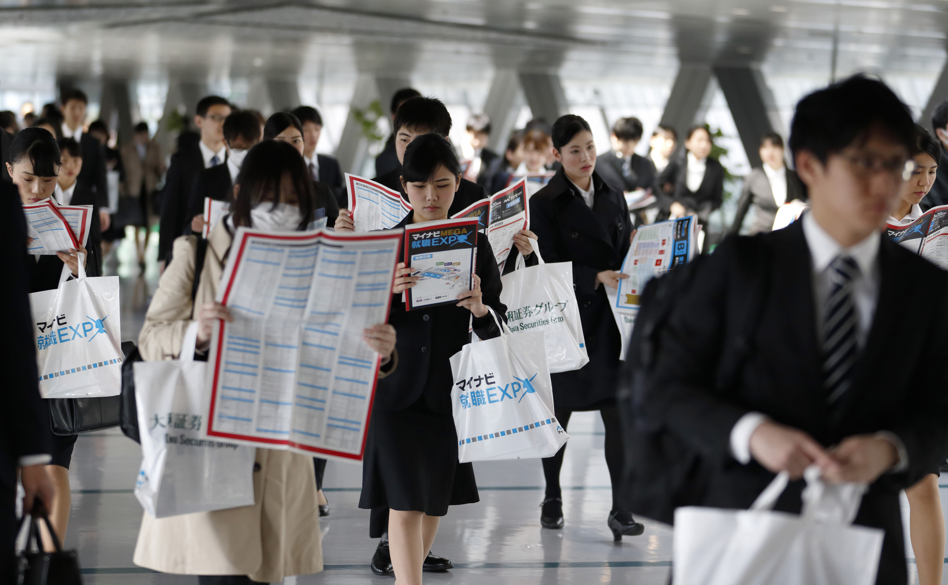 University students hold floor maps as they walk through a job fair in Tokyo. | BLOOMBERG