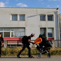 People who were sent out during a police operation to evacuate a makeshift camp at the Greek-Macedonian border near the village of Idomeni walk in front of a camp in the village of Oreokastro, Greece, Tuesday. | REUTERS