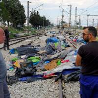 Workers stand on railway tracks during a police operation to evacuate a migrants\' makeshift camp at the Greek-Macedonian border near the village of Idomeni Thursday. | REUTERS