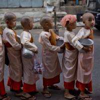 Young Buddhist nuns-in-training stand in front of a house to collect alms in Yangon on Thursday. | AP