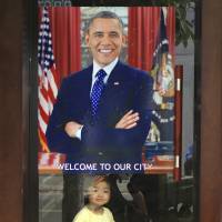 A young girl looks out and smiles under a poster of U.S. President Barack Obama hung on the door of a shop in Hanoi on Sunday, ahead of his historic visit to the Southeast Asian nation. | AP