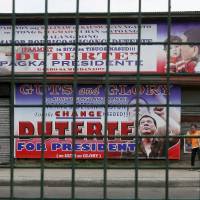 Residents walk past giant tarpaulins of presumptive President-elect Rodrigo Duterte at his hometown in Davao city, southern Philippines, on May 11. A bold campaign promise to eradicate crimes and corruption within six months and his iron-fist approach to law and order helped catapult the longtime mayor to the presidency, but Duterte\'s anti-crime reputation is also a political baggage that would haunt him now as he comes under the spotlight. | AP