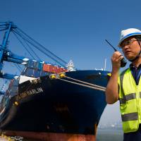 A docker stands near a container ship as it is unloaded in Busan, South Korea, in July 2015. | BLOOMBERG