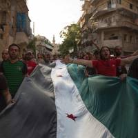 Syrians carry a giant pre-Baath Syrian flag as they shout slogans during an anti-regime protest in the rebel-held Bustan al-Qasr district in eastern Aleppo on Thursday. | AFP-JIJI