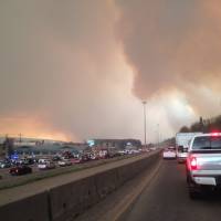 Smoke from a wildfire rises as cars line up on a road in Fort McMurray, Alberta, Tuesday. At least half of the northern Alberta city was ordered evacuated Tuesday as the wildfire whipped by winds engulfed homes and sent ash raining down on residents. | GREG HALINDA / THE CANADIAN PRESS VIA AP