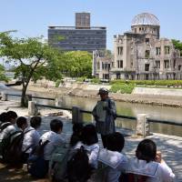 A volunteer at Peace Memorial Park in Hiroshima explains the devastation caused by the U.S. atomic bombing of the city to visiting students on May 17. | SATOKO KAWASAKI
