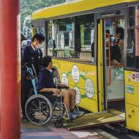 A man in a wheelchair rides a loop bus in Nara Prefecture. A new law requires government agencies and private businesses to remove “social barriers” for people with impairments, including ensuring their access to public transportation. New law bans bias against people with disabilities, but shortcomings exist, say experts