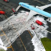 Firefighters hose down the port engine of a Korean Air Boeing 777-300 Friday on runway C at Haneda airport. | KYODO