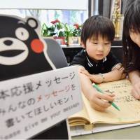 Kazuya Matsumoto, 6, and his sister Saya, 10, write messages to Kumamon at Kumamoto\'s souvenir and tourist information shop in the city of Kumamoto on Wednesday. | KYODO